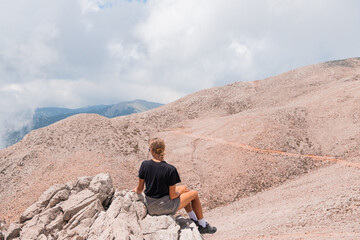 The girl is sitting on the edge of a high mountain in the clouds. The girl looks at the beautiful mountain landscape of Antalya, Turkey