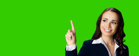 Young brunette woman in black confident suit showing pointing at copy space for text or imaginary. Business ad concept. Green chroma key background.