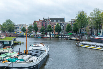 Fototapeta na wymiar Boats and houses on a canal in Amsterdam. Beautiful landscape on a cloudy day. Tourism and travel.