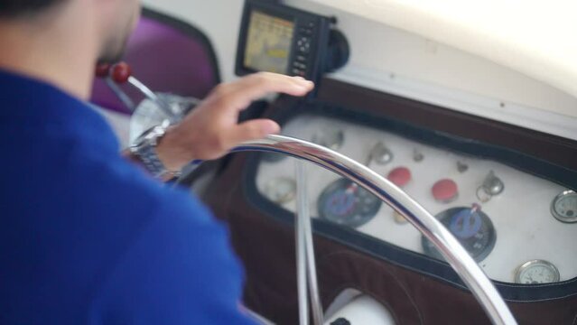 4K Caucasian man cruise ship captain holding steering hand wheel for control ship rudder and speaking on vhf radio on board while luxury catamaran boat yacht sailing in the ocean on summer vacation.