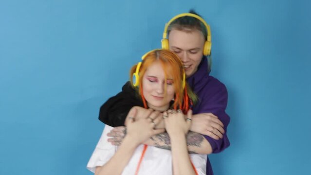 stylish modern young guy and girl listening to music hugging each other and moving slowly and smoothly on a blue background.