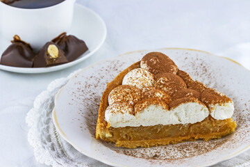 Close-up view of apple pie with cream on the plate and cup of hot chocolate behind