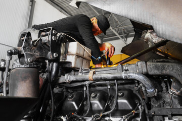 Fototapeta na wymiar Car mechanic repairs large truck or tractor in workshop. Professional mechanic repairs truck engine. Genuine worker..
