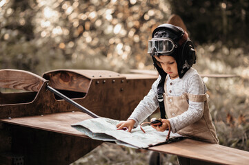 A young aviator boy near a homemade airplane in a natural landscape with a compass and a geographical map. The authentic mood of the picture. Cartography. Vintage. © Anastasia