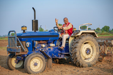Indian senior farmer sitting on tractor at agriculture field.
