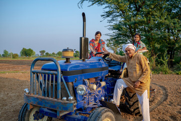 Indian senior farmer sitting on tractor with family. Indian rural family.