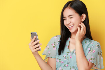 Image of joyful charming asian woman laughing and use smart phone isolated over yellow background