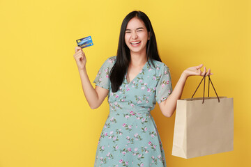 young asian woman standing with credit card and a bunch of shopping bags in hands on yellow background