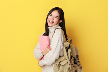 happy young Asian woman student with backpack holding notebook on yellow background