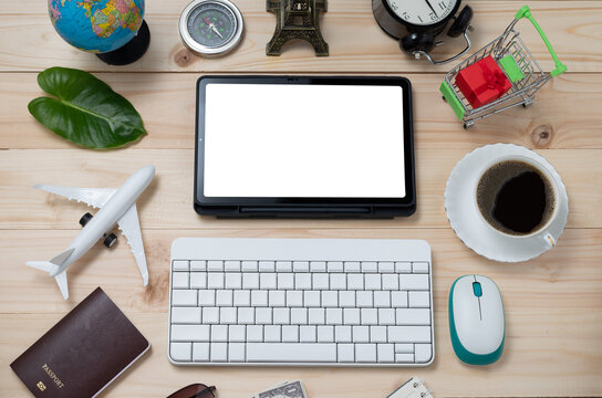Travel and business concept with keyboard accessories and passport on rustic wooden table background. Vacation Globe, cup, cart, airplane, compass, and tablet blank screen for text. Top view.