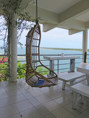 Rattan wicker cocoon swing chair on porch with ocean view