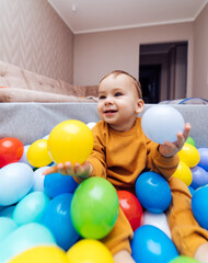 Cute little infant playing with colorful balls in dry pool. Little cute baby having fun in ball pit on birthday party at home.
