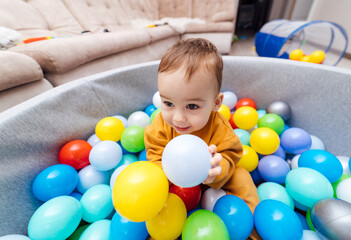 Fototapeta na wymiar Happy boy playing in colorful balls pool. Ball pit. Activity toys for little kid.