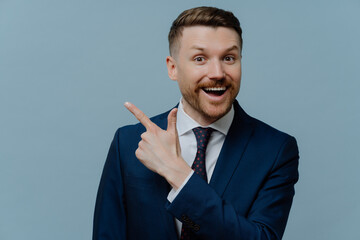Happy successful male entrepreneur with bristle dressed in formal clothes points at upper right corner demonstrated place for your advertisement gives advice how to start own business. Office style
