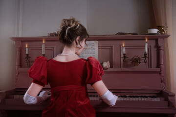 Young girl in a red vintage dress from the 19th century plays the piano - obrazy, fototapety, plakaty