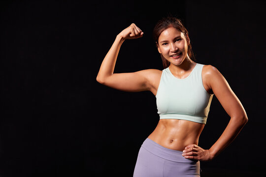 portrait young woman trainer smiling and flexing both arms muscles on black background