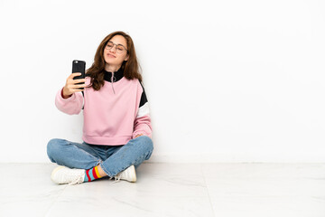 Young caucasian woman sitting on the floor isolated on white background making a selfie