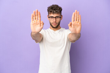 Delivery caucasian man isolated on purple background making stop gesture and disappointed