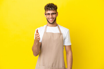 Restaurant waiter blonde man isolated on yellow background shaking hands for closing a good deal