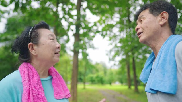 Asian cheerful happy retirement aged people talking while resting after jogging inside the green recreational park. Concept of health care for old age, Elderly love care for each other healthy outdoor