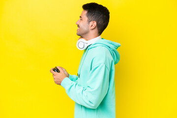 Young handsome man playing with a video game controller over isolated wall laughing in lateral position