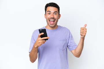 Young handsome man over isolated white background using mobile phone while doing thumbs up