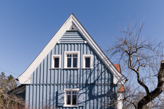 blau gestrichenes Holzhaus mit weiß eingefasten Fenstern vor wolkenlosem Himmel