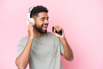 Young Brazilian man isolated on pink background listening music with a mobile and singing