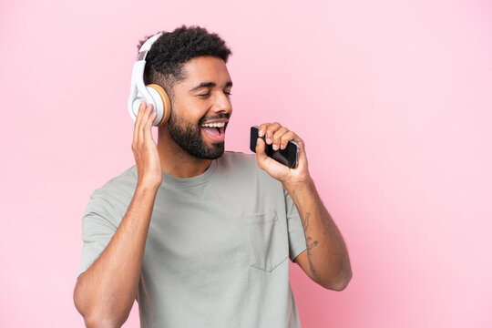 Young Brazilian man isolated on pink background listening music with a mobile and singing