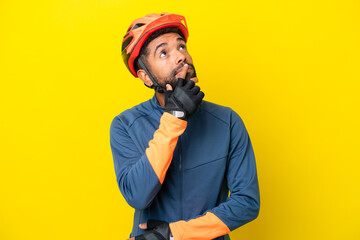 Fototapeta premium Young cyclist Brazilian man isolated on yellow background having doubts while looking up