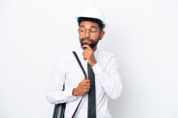 Young architect Brazilian man with helmet and holding blueprints isolated on white background having doubts and thinking