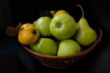 still life of apples, pears and quince in a basket on a black background

