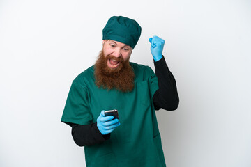 Surgeon redhead man in green uniform isolated on white background surprised and sending a message