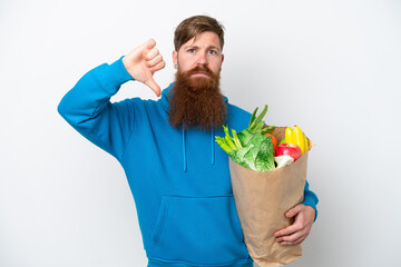 Redhead man with beard holding a grocery shopping bag isolated on white background showing thumb down with negative expression