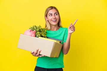 Young Uruguayan girl making a move while picking up a box full of things isolated on yellow...