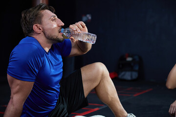 muscular man or trainer drinking water in gym after workout