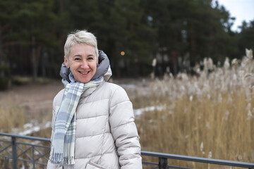 Fototapeta premium Portrait of happy beautiful elderly senior retired woman in age outdoors in forest or park at winter cold day, smiling and calm enjoy weather