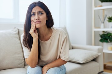 Woman toothache, tooth root inflammation sitting on sofa at home
