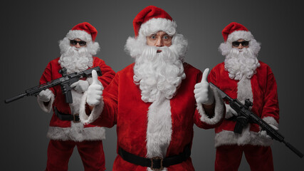 Portrait of three santa dressed in red costume and two with santa bodyguards rifles.