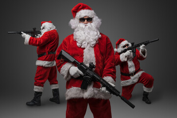 Studio shot of stylish crew of three santa with rifles isolated on grey background.