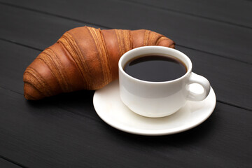 Black coffee with a fresh croissant on a black wooden background