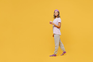 Fototapeta na wymiar Full body side view young woman she wear purple pyjamas jam sleep eye mask rest relax at home hold takeaway delivery craft paper cup coffee to go isolated on plain yellow background Night nap concept