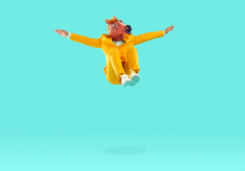 Man with dinosaur head jumping in air on yellow background. Funny man in yellow suit jumping high...