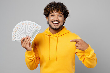Young rich fun wealthy Indian man 20s wear casual yellow hoody hold in hand point finger on fan of...