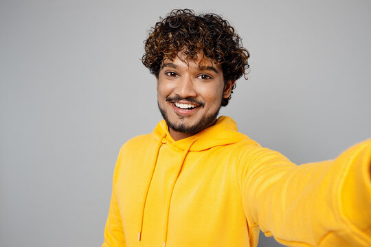 Close Up Young Smiling Happy Fun Indian Man 20s He Wearing Casual Yellow Hoody Doing Selfie Shot Pov On Mobile Cell Phone Isolated On Plain Grey Background Studio Portrait. People Lifestyle Portrait