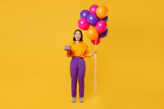 Full body happy smiling fun young woman wears casual clothes celebrating holding in hand cake with candles bunch of balloons isolated on plain yellow background. Birthday 8 14 holiday party concept.