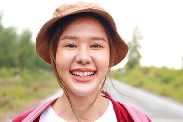 Portrait of a beautiful Asian woman wearing a hat and carrying a backpack She smiles cheerfully and enjoys nature tourism. Travel concept. Tourists hiking, camping