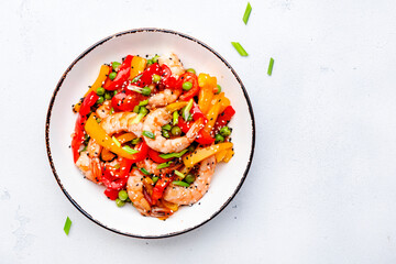 Stir fry with shrimps, red and yellow paprika, green pea, chives and sesame seeds in white bowl Asian cuisine dish. Light stone kitchen table background, top view