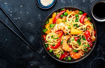 Stir fry noodles with shrimps, red and yellow paprika, green pea, chives and sesame seeds bowl. Asian cuisine dish. Black stone kitchen table background, top view