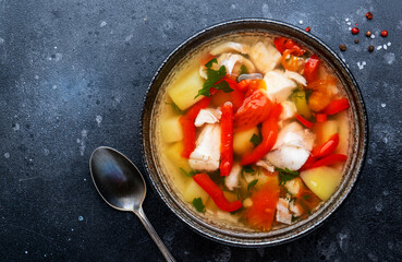 Fish soup with cod, paprika, potatoes, tomatoes and parsley in ceramic soup bowl on dark table background, top view